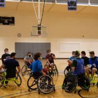 Group of adults in wheelchairs facing each other in a circle holding basketballs.